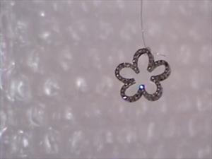 A small, sparkly flower gem hangs from fishing wire in front of a bubble-wrapped background.